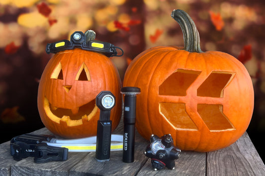 2 carved pumpkins sitting next to each other on a wood surface. One with a face and the other with the STKR Concepts logo carved out of it. Sitting in front of them are a couple STKR lights.