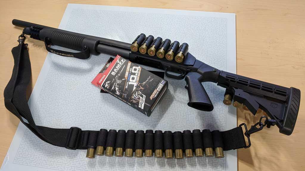 Tactical shotgun with a pistol grip, adjustable stock, and shell holders, displayed on a table alongside a sling loaded with shells. A box containing a BAMFF Tactical Flashlight by STKR is placed beneath the shotgun.
