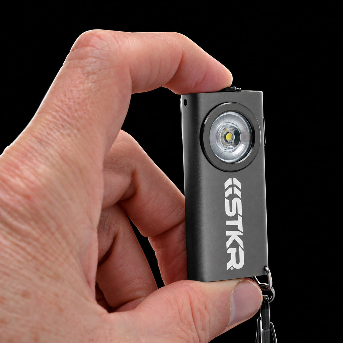 Gray STKR SlimJIMMY keychain light held between two fingers to show its size