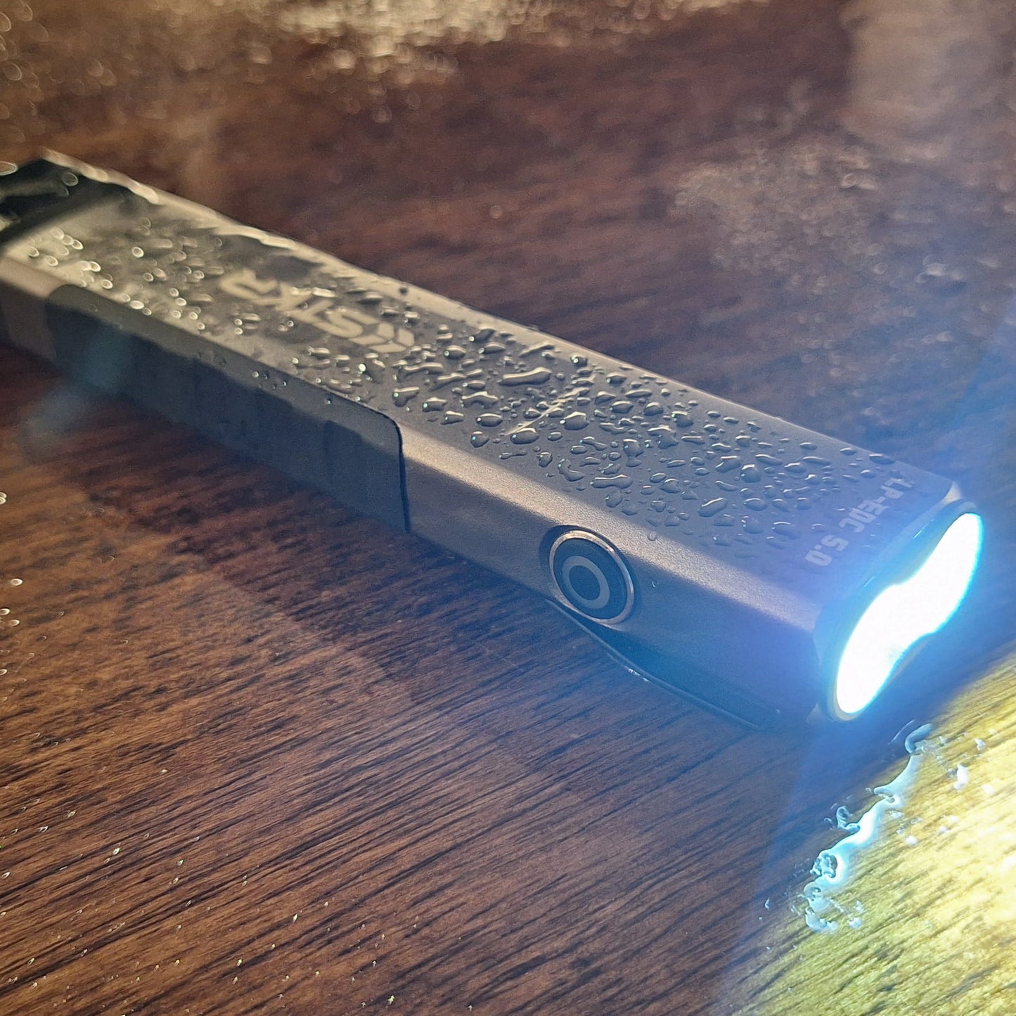 LP-EDC 5.0 Low Profile Everyday Carry Ultra-Thin Flashlight sitting on a wood surface covered in water droplets